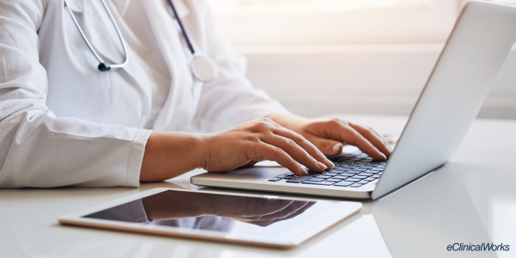 Doctor typing on laptop computer on desk with iPad next to the computer. eClinicalWorks logo in the lower right corner.