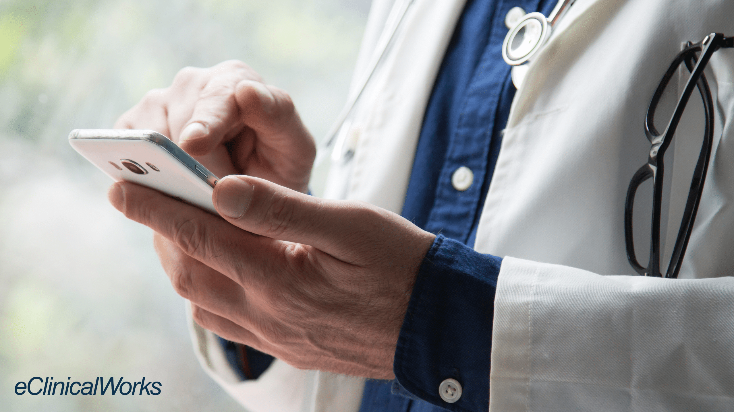 doctor holding and using smartphone and the eclinicalworks logo in the lower left corner