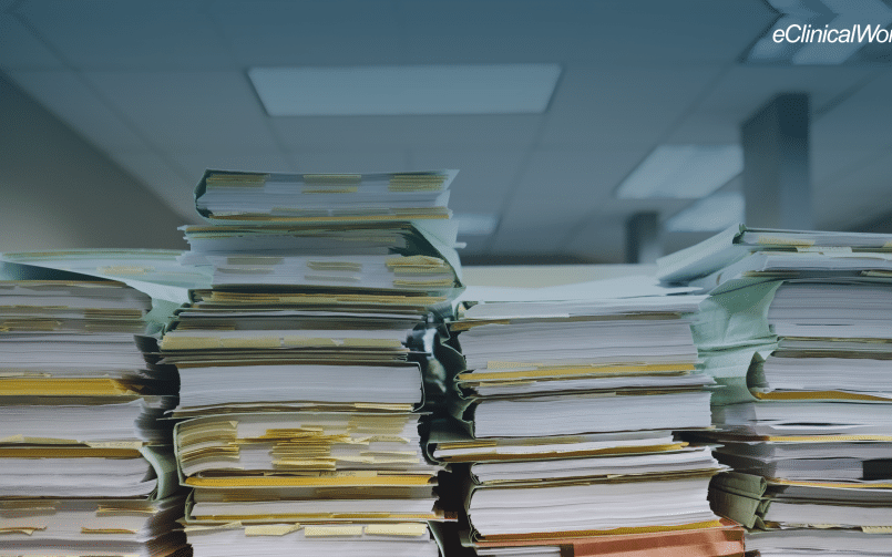 stack of books with sticky notes and files with a blue gradient on the top half of the image and the eClinicalWorks logo in the upper right hand side in white text