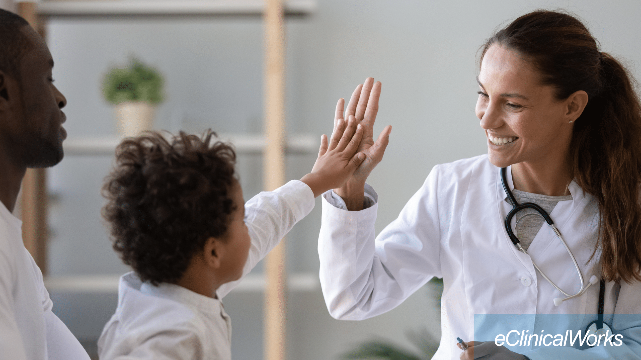 Provider high-fiving child patient in lap of parent with the eClinicalWorks logo in white in the lower right corner
