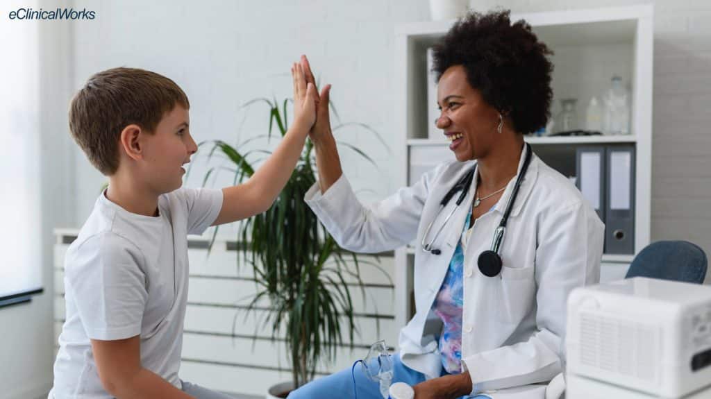 Female doctor high fiving a young male patient. They're both smiling looking engaged.