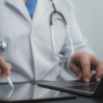 Doctor working at laptop and ipad, icon of Image AI fax from eClinicalWorks on screen.