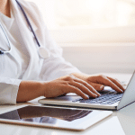 doctor sitting at laptop typing representing electronic health records (EHR)